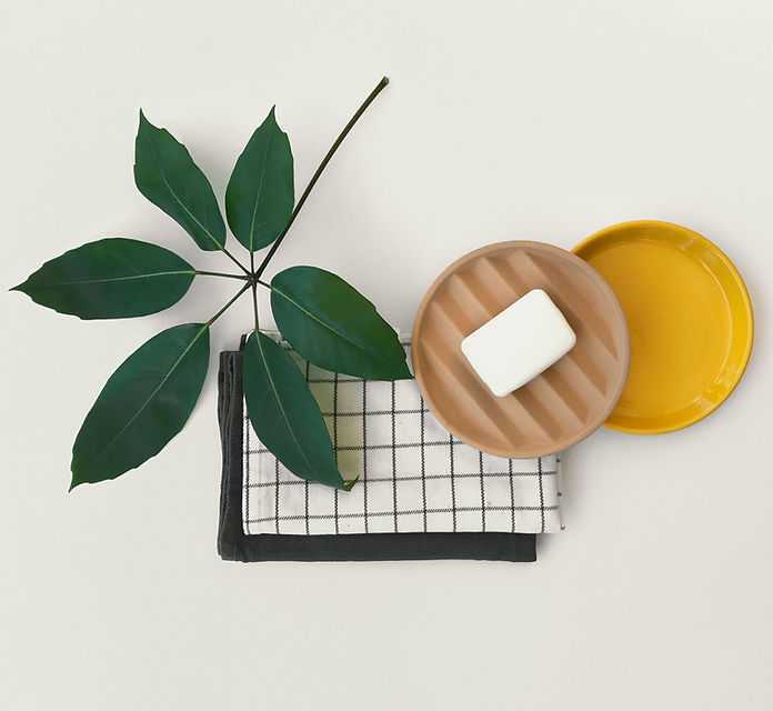 Leaf, checkered towel, and soap on ceramic dishes arranged on a light background.