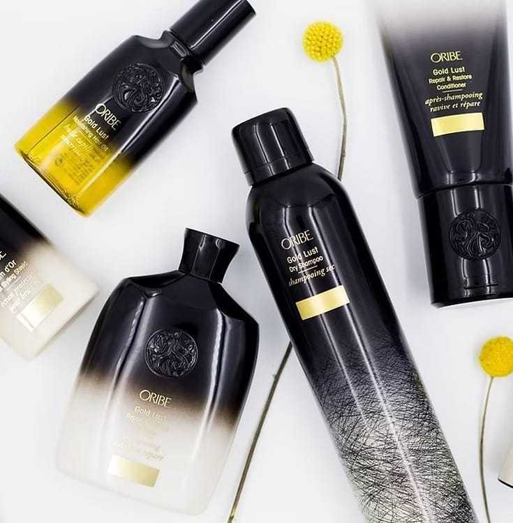Luxury hair care products from Oribe displayed on a white background with yellow flowers.