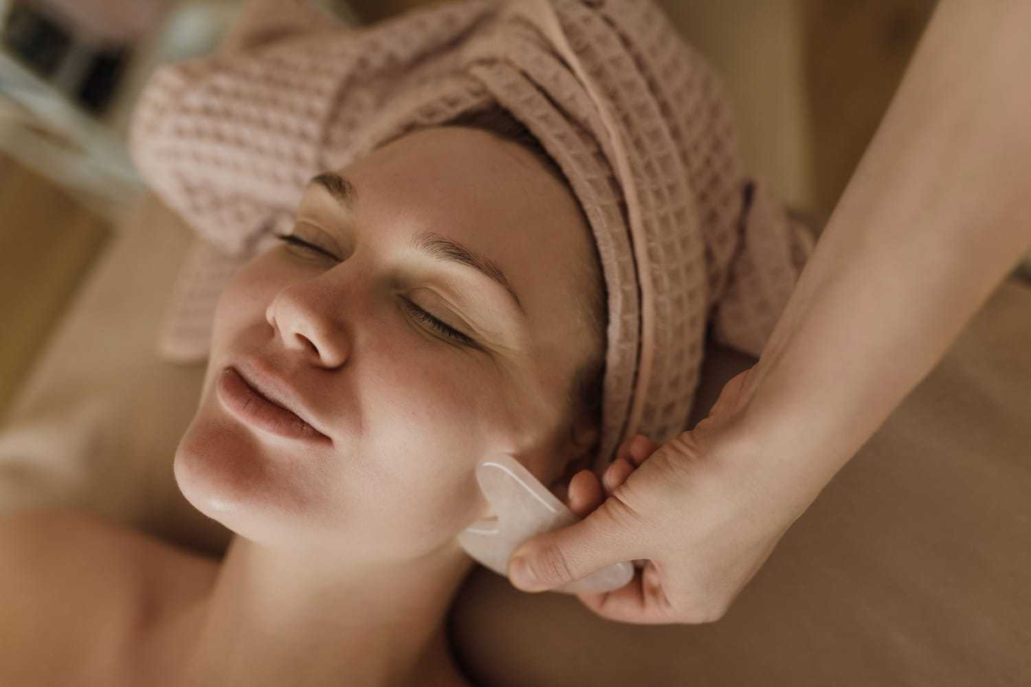 Woman receiving facial massage with a gua sha tool in a spa setting.