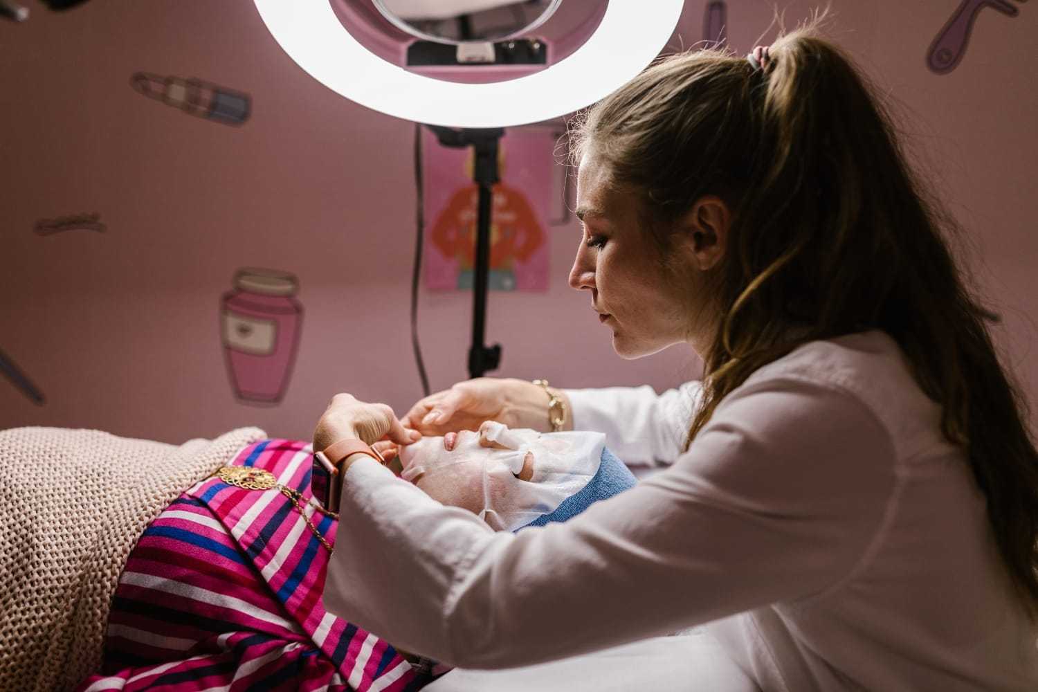 Woman receiving facial treatment under ring light in a spa room.