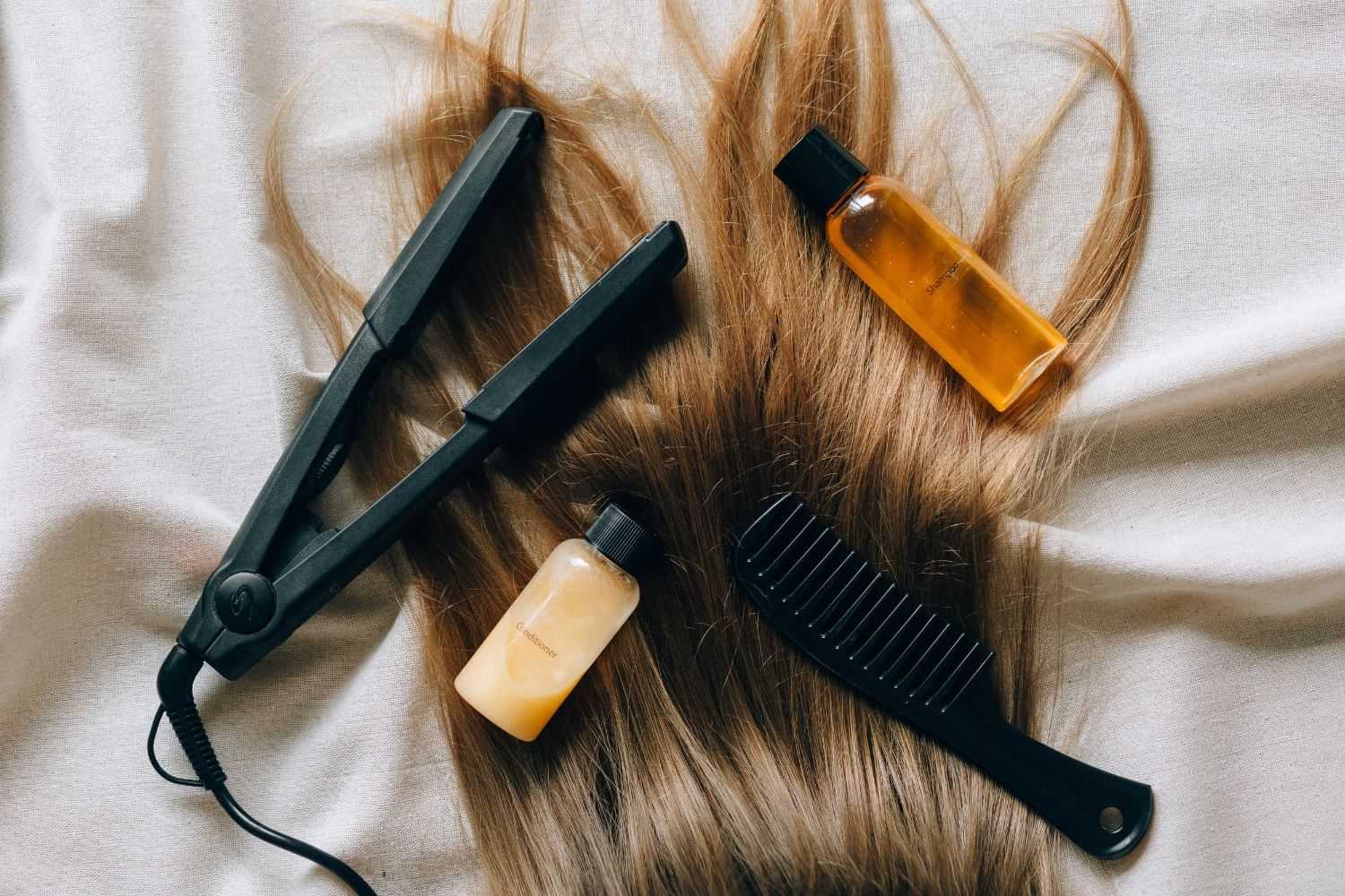Hair styling tools and products displayed on long, brown hair laid out on a white surface.